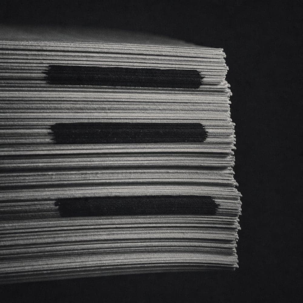 The cut edge of a stack of printed documents with three lines redacted.